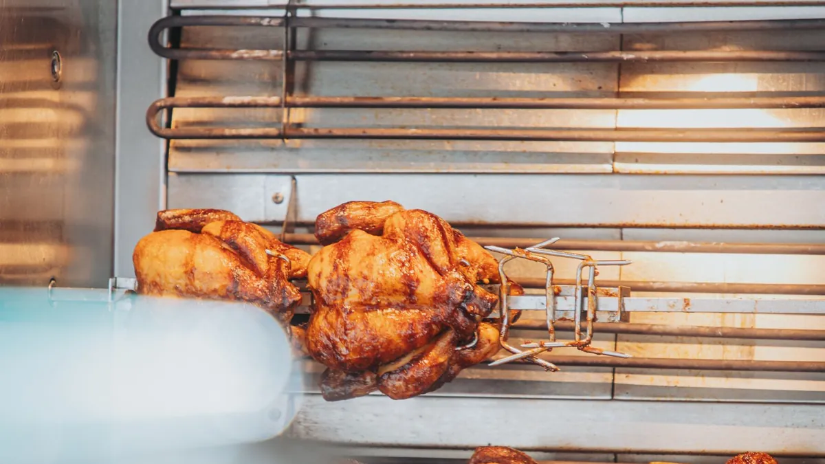 Rotisserie chicken turning slowly on a grill spit, skin golden and crisp