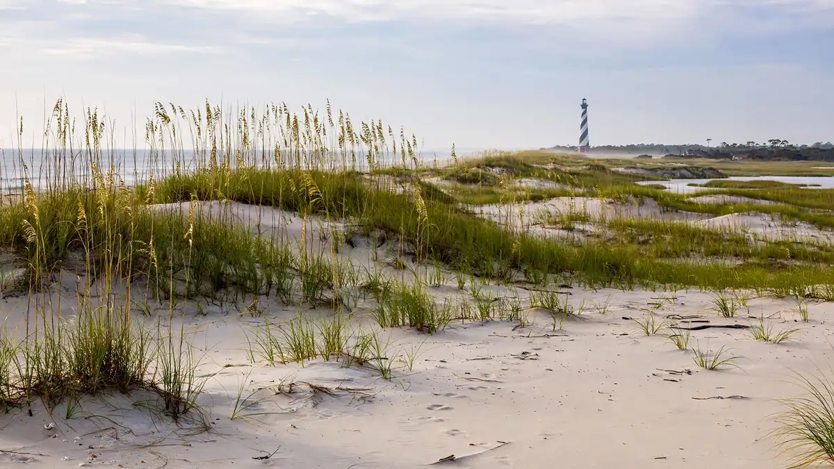 Wide sandy beach in the Outer Banks NC with dunes, sea oats and a lighthouse in the distance under soft Atlantic light