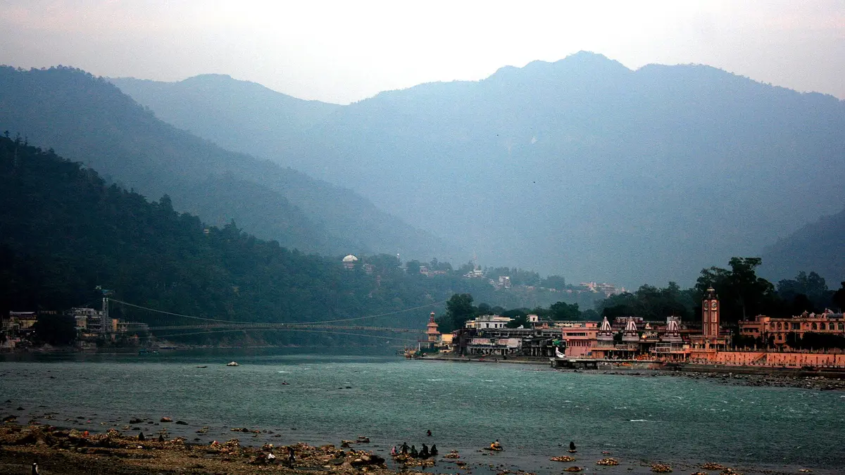 Ram Jhula suspension bridge over the Ganges river in Rishikesh with ghats and hills