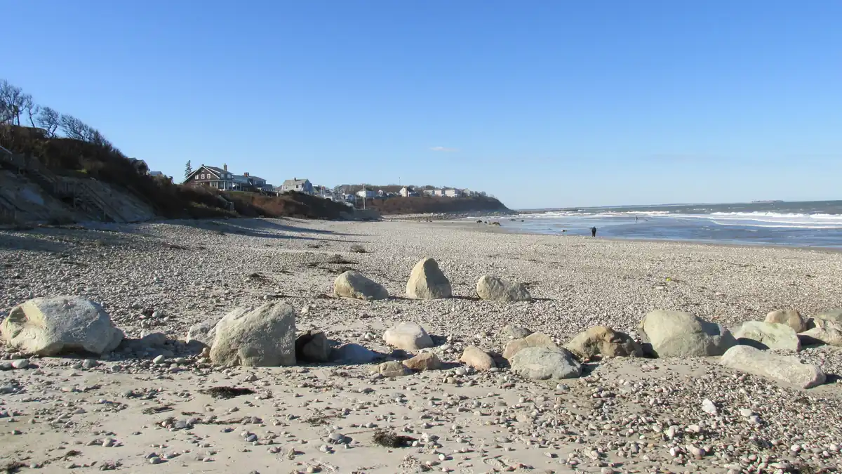 Priscilla Beach in Manomet, Plymouth, Massachusetts, with boulders on the pebbly sand, beach houses on the bluff, and Cape Cod Bay beyond