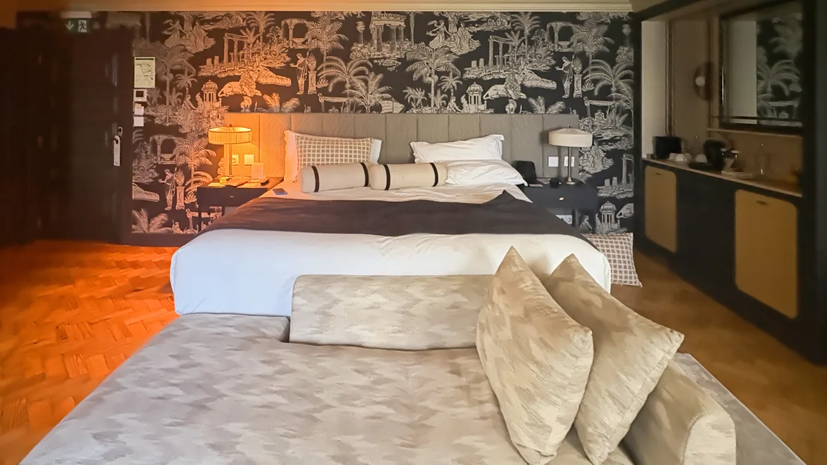 Design-led boutique hotel room in Lisbon with bold tropical wallpaper, a comfortable bed, and warm natural light