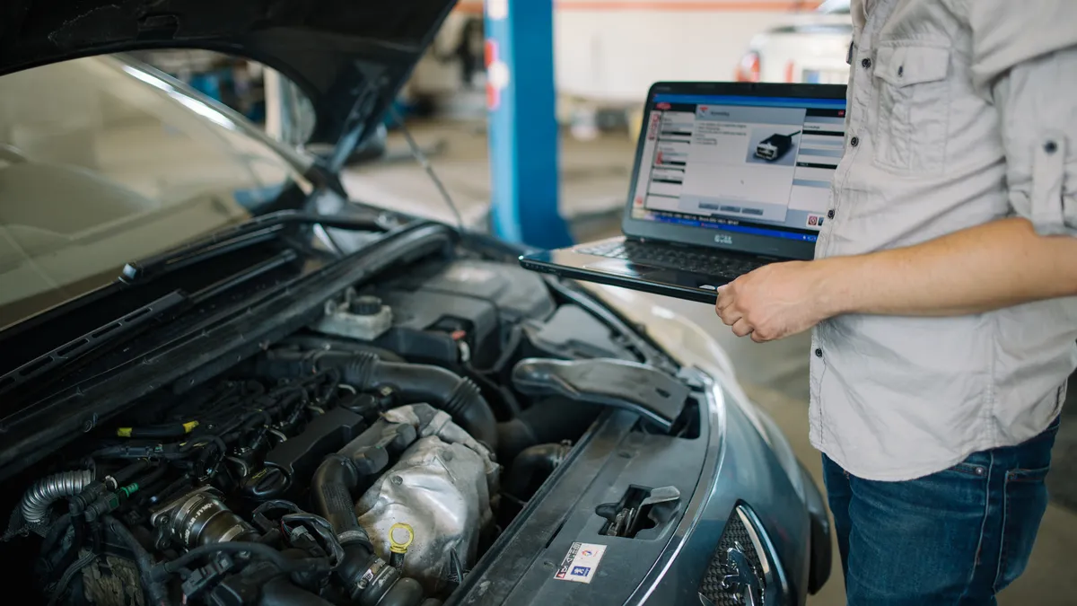 Mechanic with a laptop carrying out car diagnostics on a vehicle in an auto repair shop, illustrating expert auto service and fault-finding