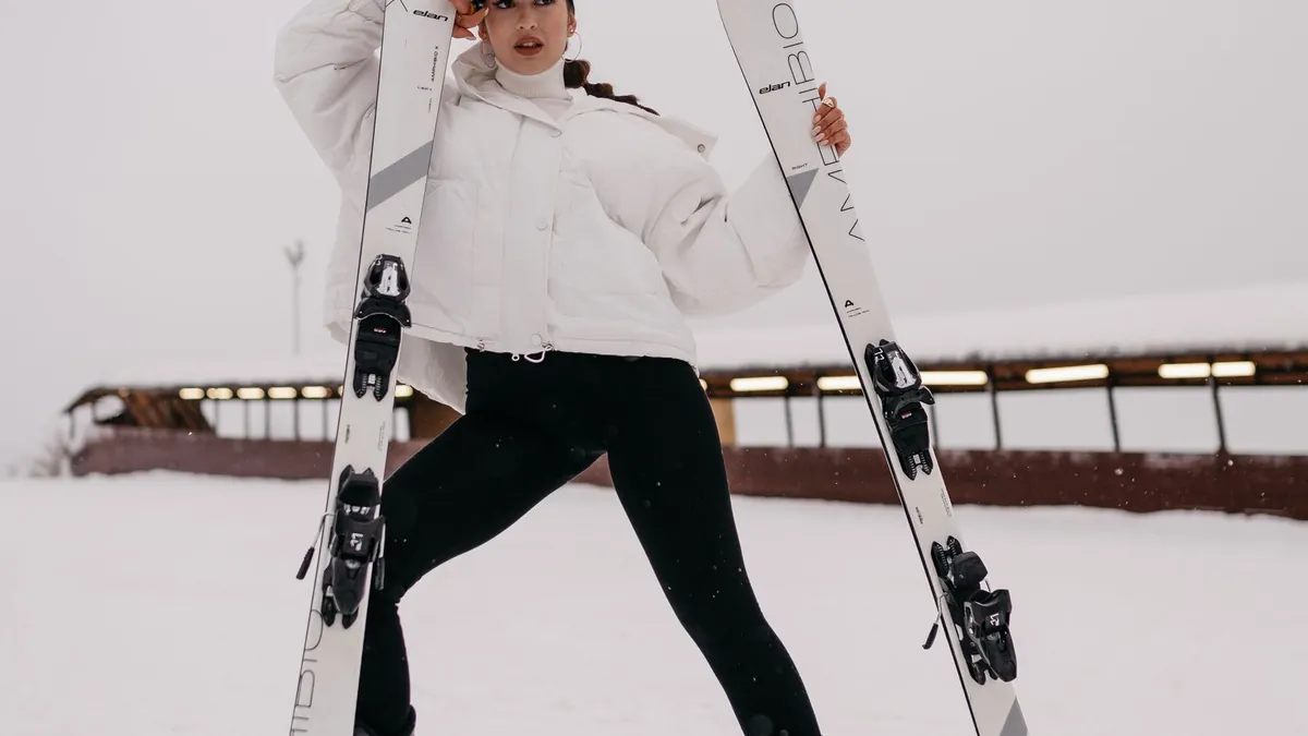 Stylish woman in ski gear posing confidently with her skis in a snowy alpine landscape