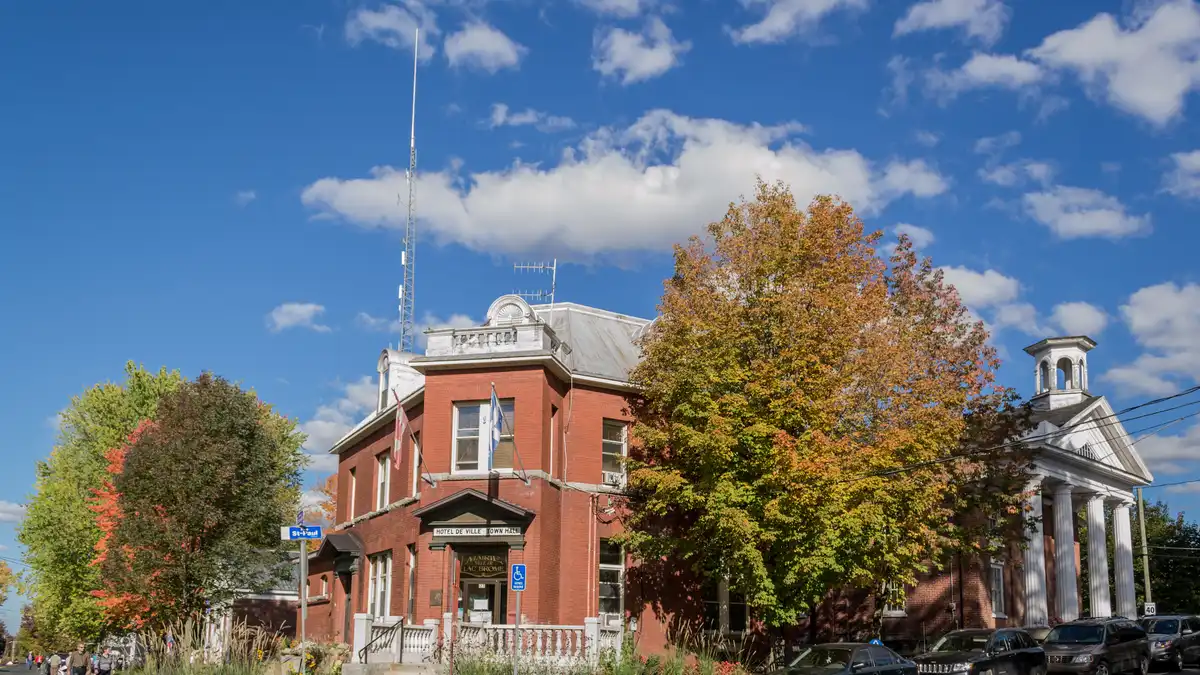 The red-brick Brome Lake Town Hall in Knowlton, Quebec, with the white-columned Old Court House beside it under autumn trees