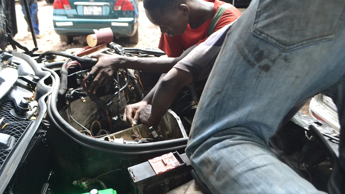 Two mechanics working together on a car engine during a service visit in a workshop