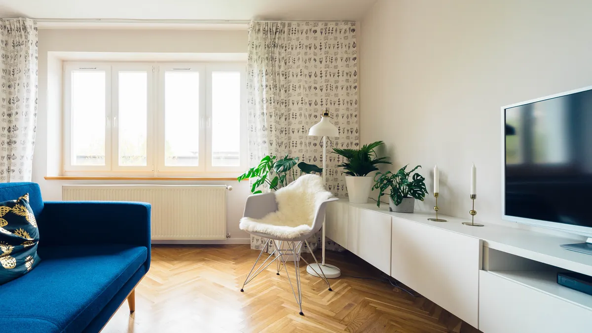 Bright modern living room with a long white low media console along the wall, a large flat-screen TV, houseplants and a blue sofa