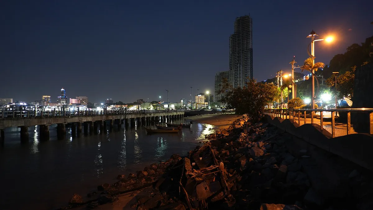A waterfront promenade at night with streetlights glowing along the shore and city lights reflected in calm water