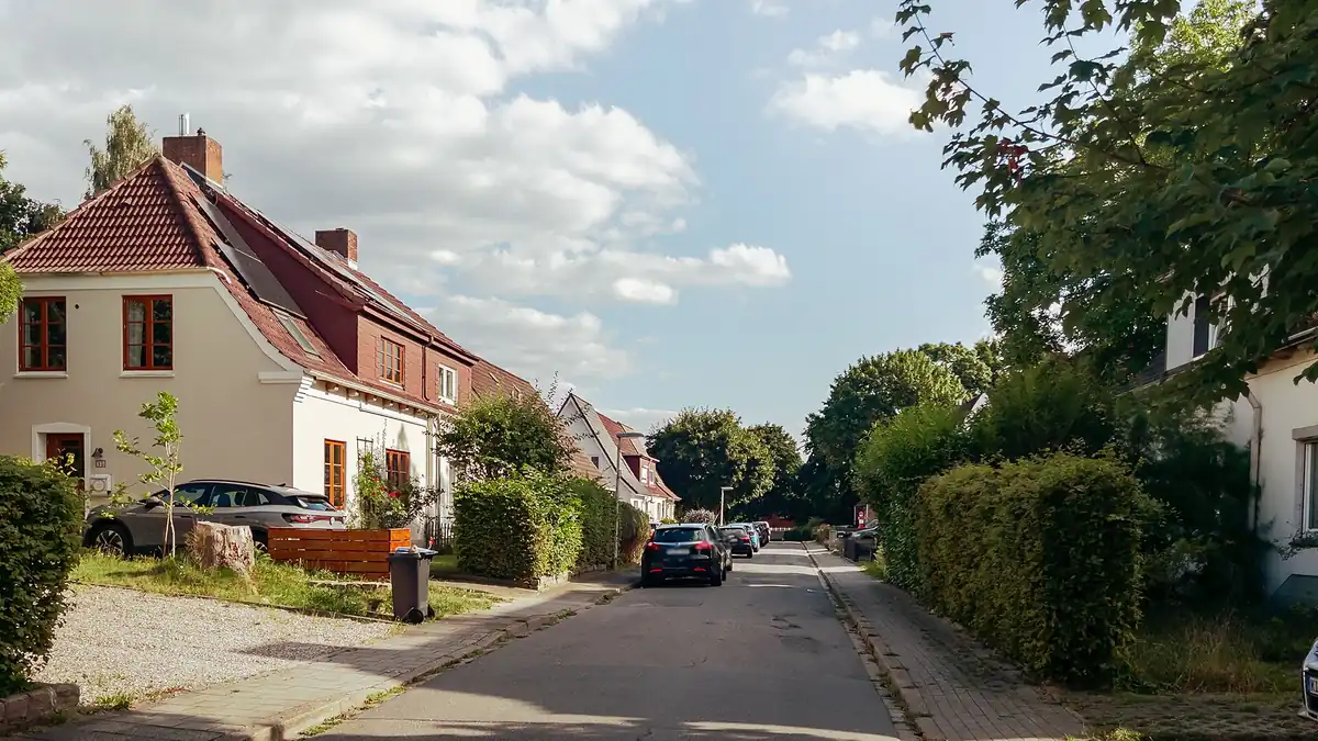 A quiet residential street with family houses, a car parked in a driveway and more cars parked along the road, representing the home and car that insurance shopping protects