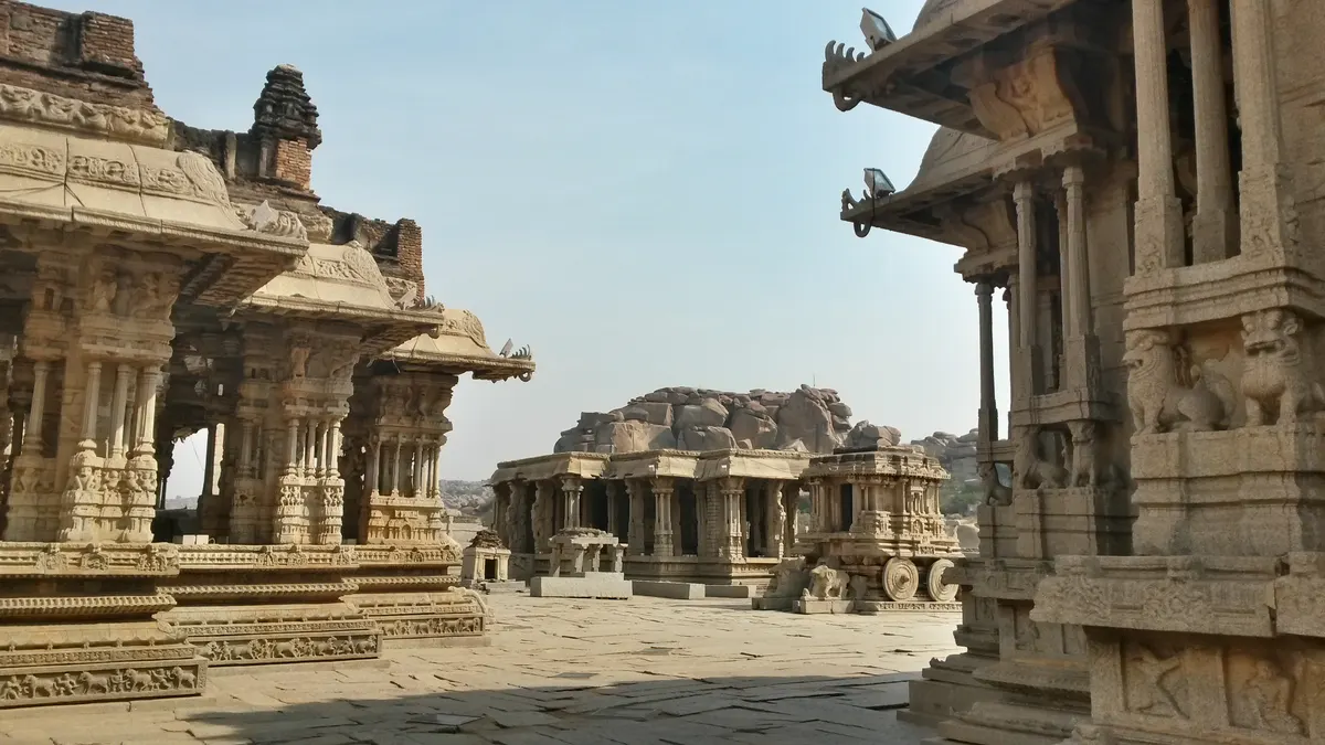 The Stone Chariot at Vittala Temple in Hampi, Karnataka, surrounded by ancient stone halls and boulders under a bright sky