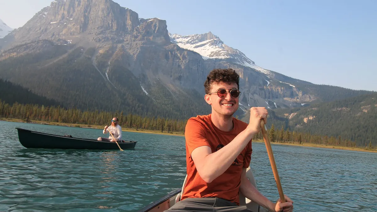 A red canoe on the vivid green water of Emerald Lake in Yoho National Park, with forested Rocky Mountain peaks behind it