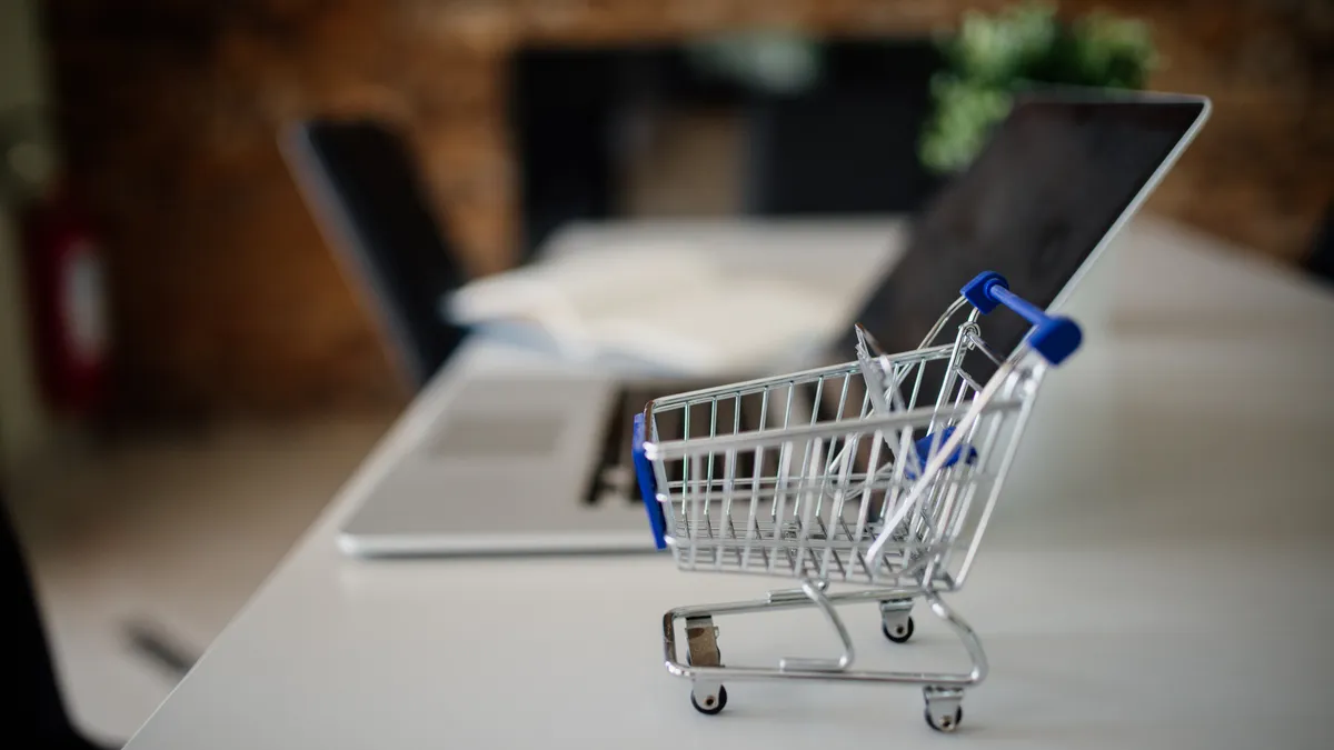 A miniature shopping cart on a desk beside a laptop in a modern office, representing online shopping and ecommerce customer acquisition
