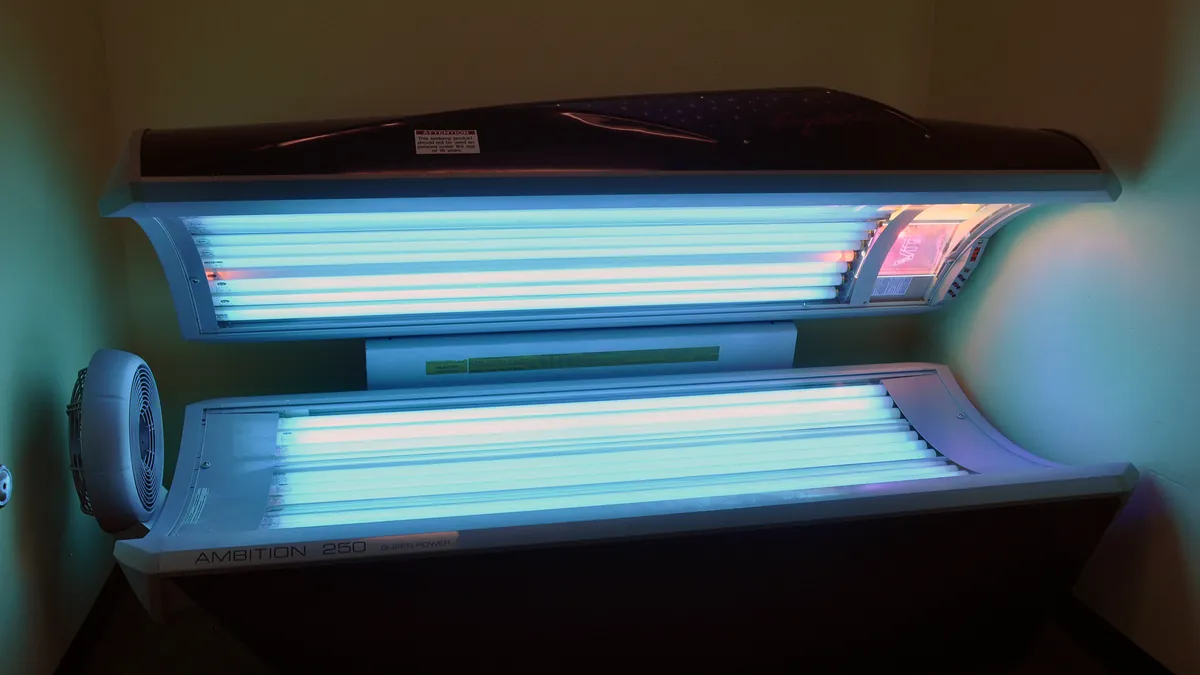 Modern tanning bed with its canopy open in a salon, showing the lamp-lined interior of current indoor tanning equipment