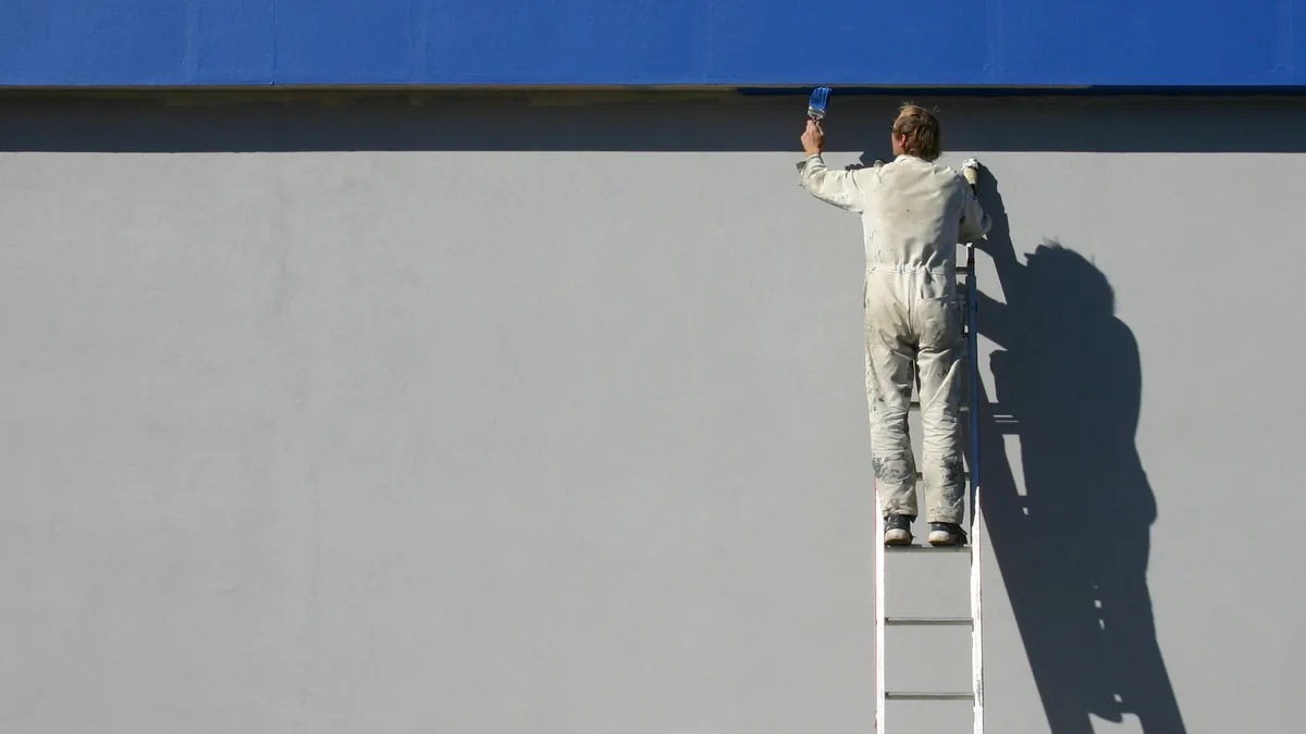 Professional painter in white overalls on a ladder painting the exterior wall of a building