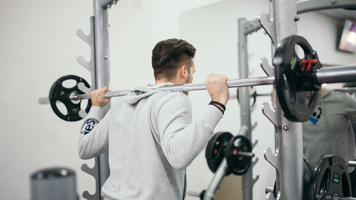 Well-groomed man performing a barbell squat during a strength training session in a gym
