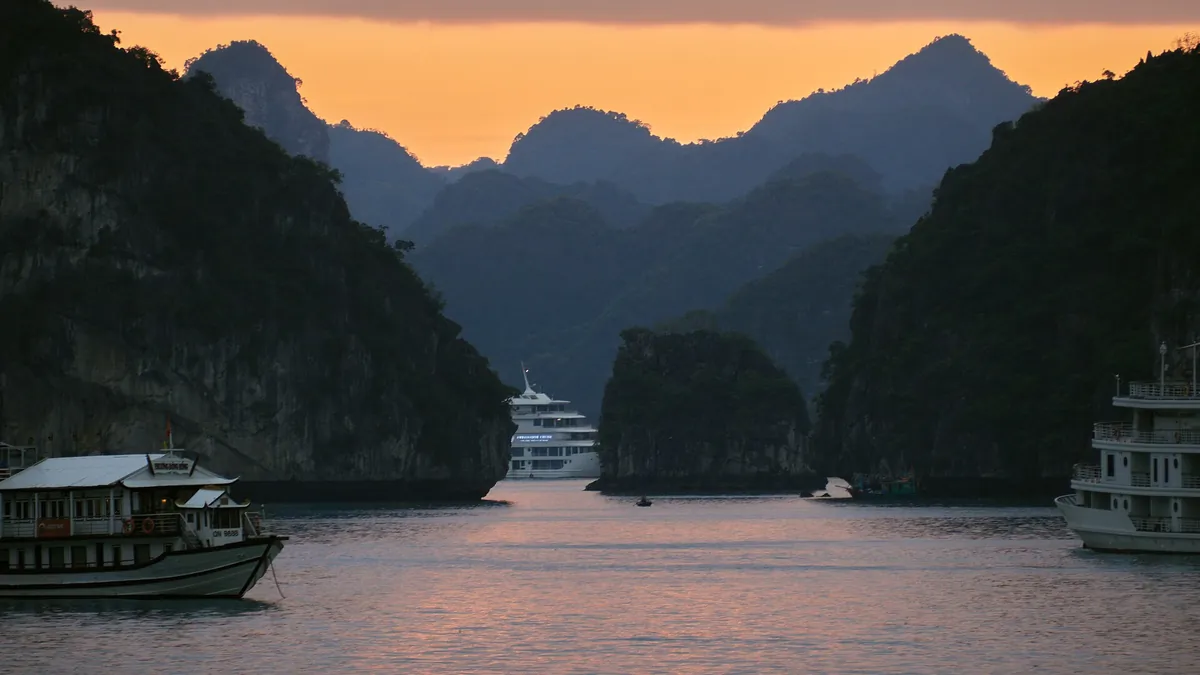 Boats among limestone karst islands in Ha Long Bay, Vietnam, under a bright sky